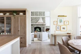 Cozy living room with stone fireplace, white sofas, wooden dining table, and framed artwork on cream walls.