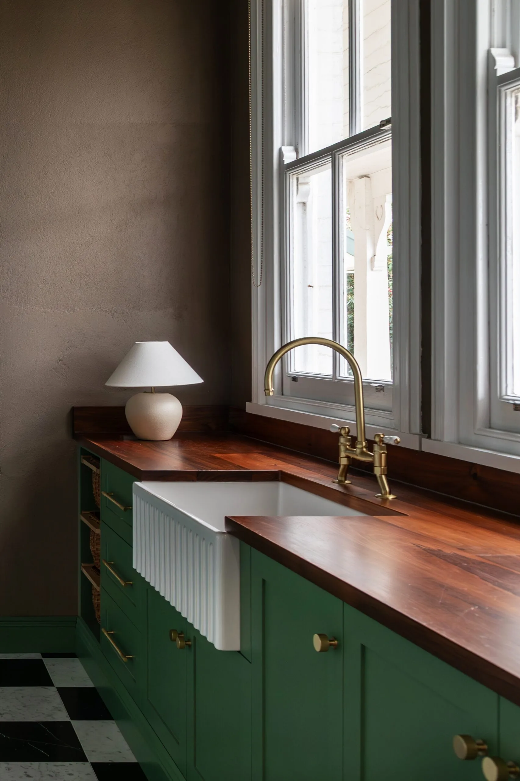 Green laundry with fluted white butler's sink and timber benchtop with lamp