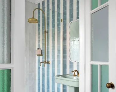 Elegant bathroom with blue and white tiles, glass shower door, brass fixtures, and a pedestal sink.