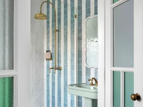 Elegant bathroom with blue and white tiles, glass shower door, brass fixtures, and a pedestal sink.