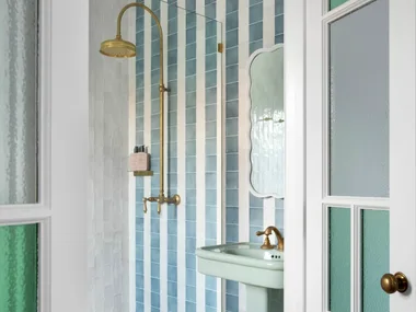 Elegant bathroom with blue and white tiles, glass shower door, brass fixtures, and a pedestal sink.