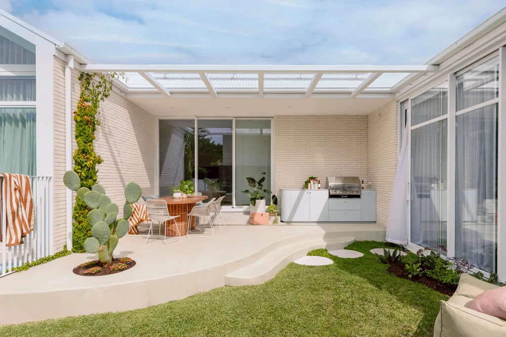 Outdoor kitchen with a cactus, round table, chairs, greenery, and a barbecue on a sunny day.