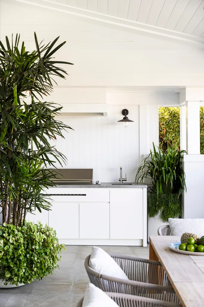 Outdoor kitchen with white cabinets, plants, and a wooden dining table with limes on a plate.