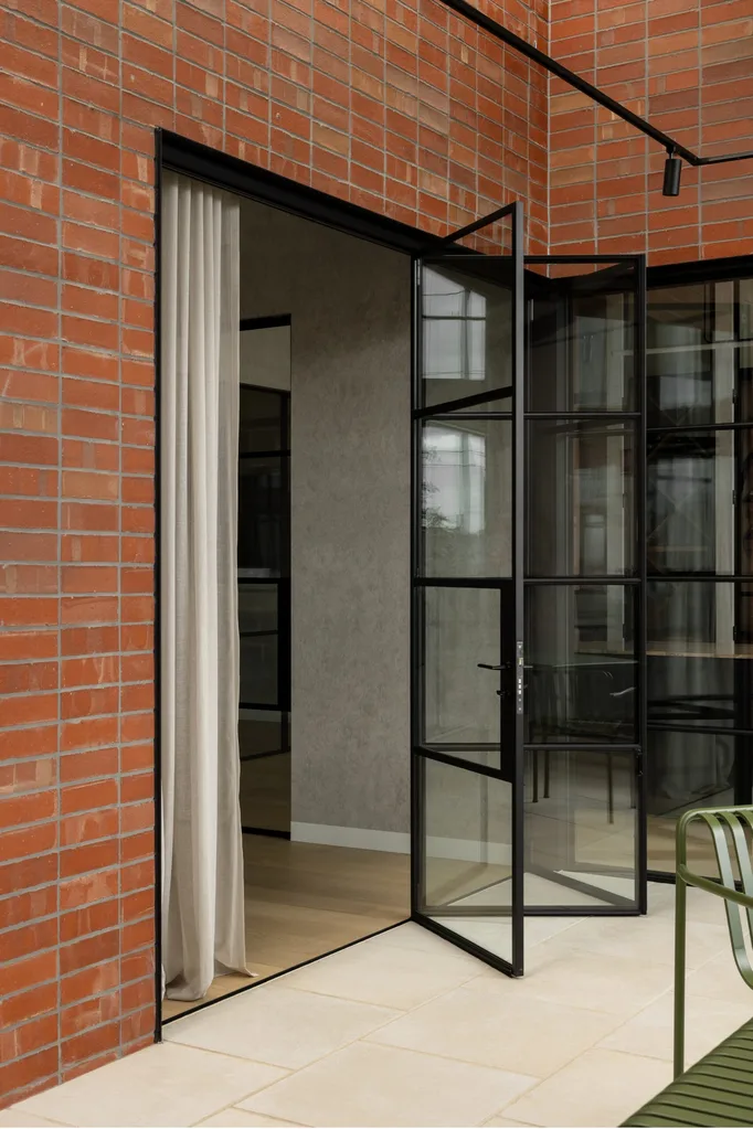Brick home exterior with black framed bifold steel doors opening out onto paved courtyard