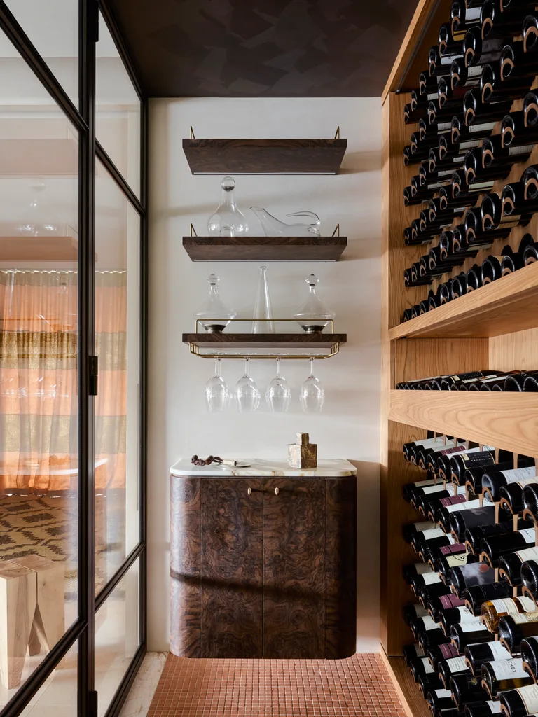 Wine cellar with shelves holding glass decanters, a cabinet below, and wine bottles on wooden racks to the right.