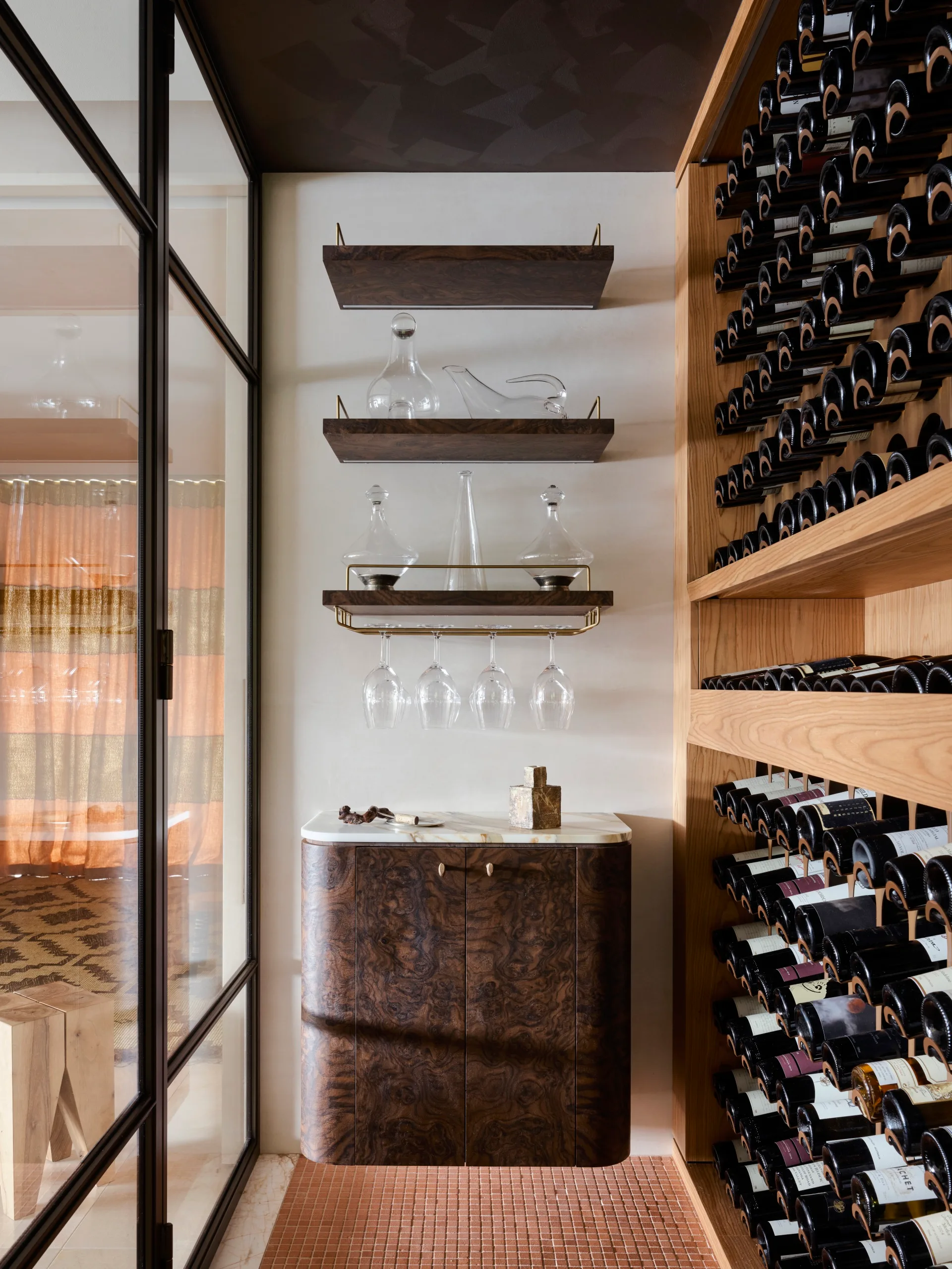Wine cellar with shelves holding glass decanters, a cabinet below, and wine bottles on wooden racks to the right.