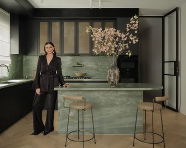 Briellyn Turton interior designer stands in a kitchen with a green marble island bench topped with cherry blossom flowers