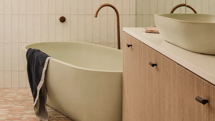 Modern bathroom with freestanding tub, towel draped over, wood vanity, pendant light, and reflective mirror.