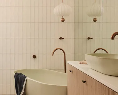 Modern bathroom with freestanding tub, towel draped over, wood vanity, pendant light, and reflective mirror.