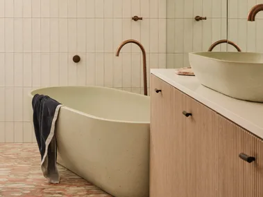 Modern bathroom with freestanding tub, towel draped over, wood vanity, pendant light, and reflective mirror.