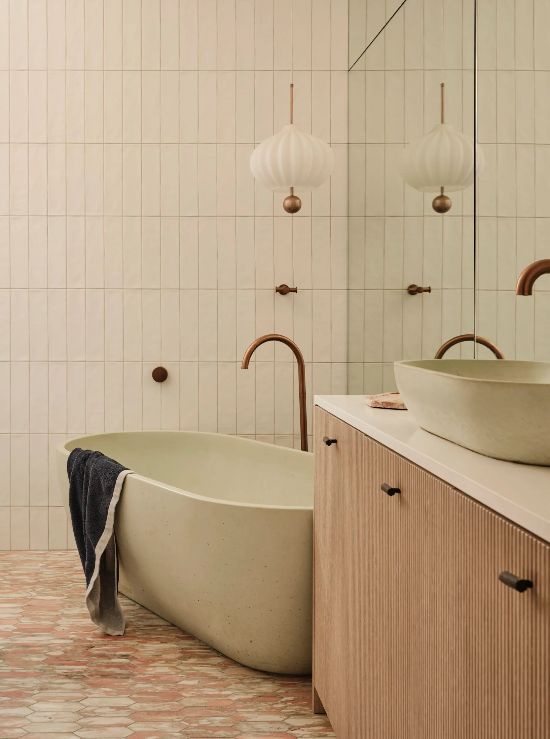 Modern bathroom with freestanding tub, towel draped over, wood vanity, pendant light, and reflective mirror. It's the main bathroom in a family home.