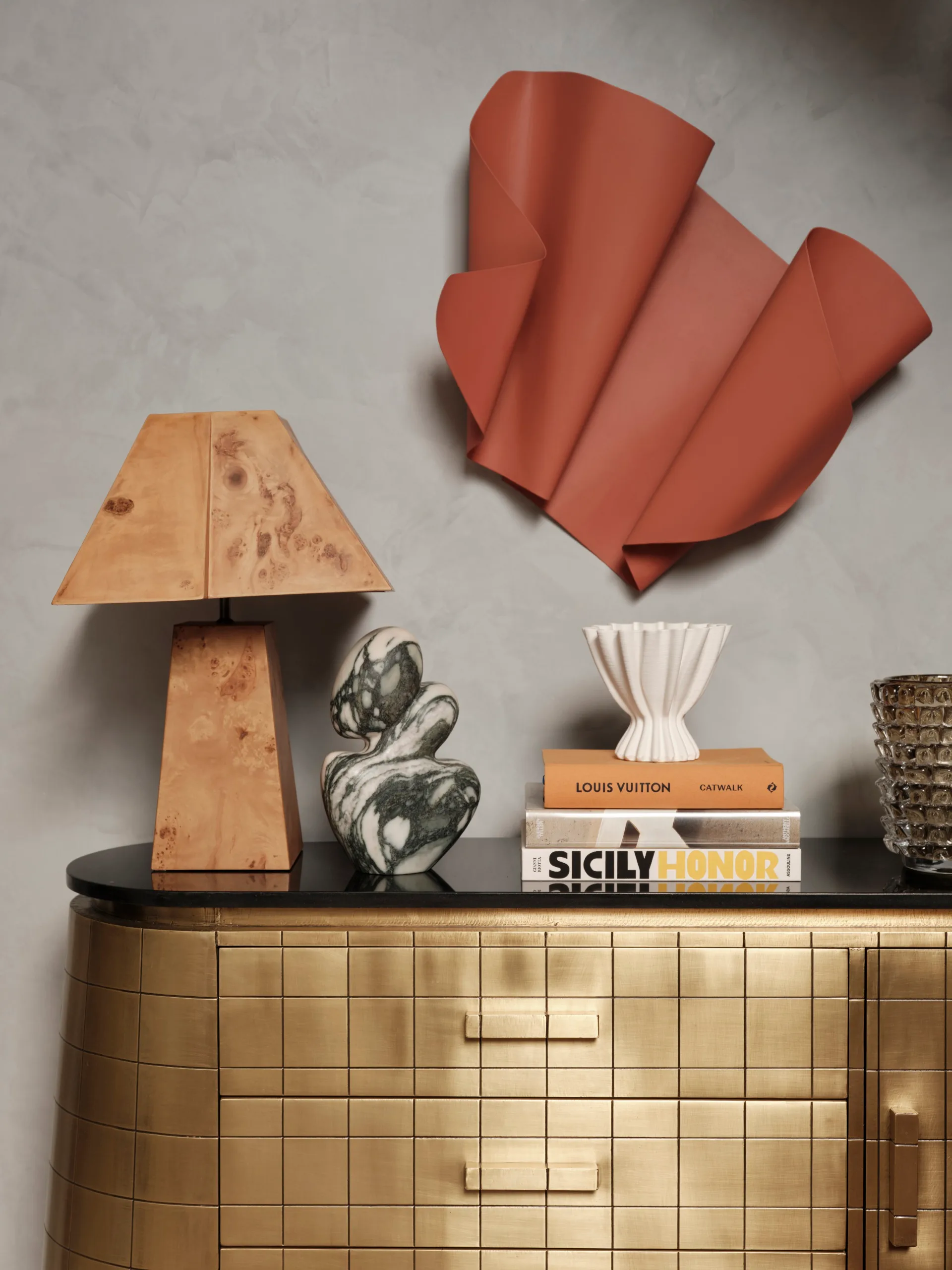 Golden dresser with decorative items including a wood lamp, abstract sculpture, books, and a red wall sculpture above.