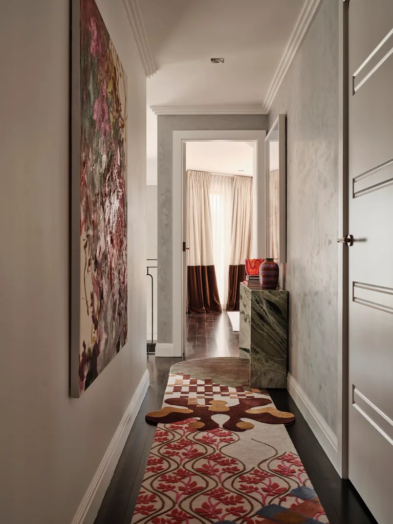 Narrow hallway with abstract artwork on the left wall, patterned carpet, and light-filled curtains at the end.