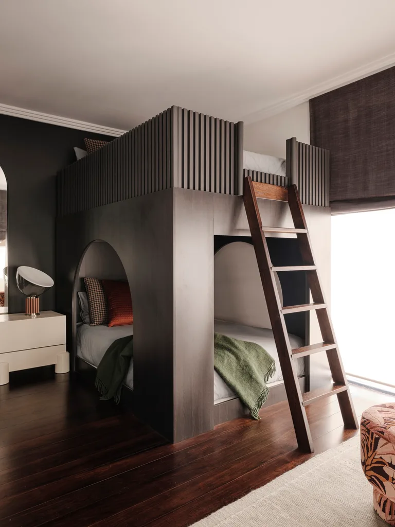 Cozy bedroom with a built-in dark wood bunk bed, ladder, green blanket, and soft lighting; modern and inviting design in a family home.