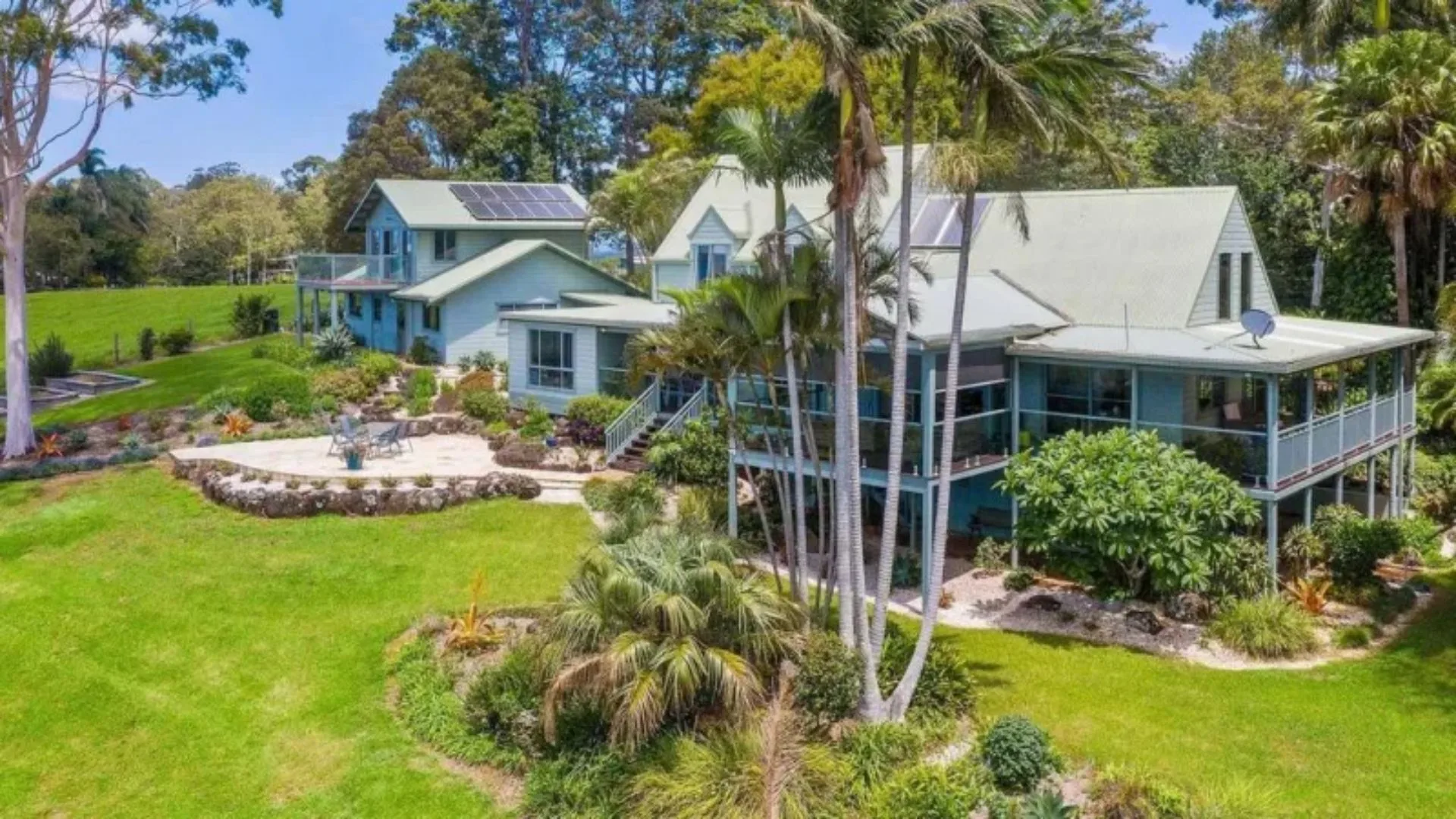 The exterior of Jacob Elordi's home showing a large two storey home on stilts with a verandah, pitched roof and manicured green gardens around