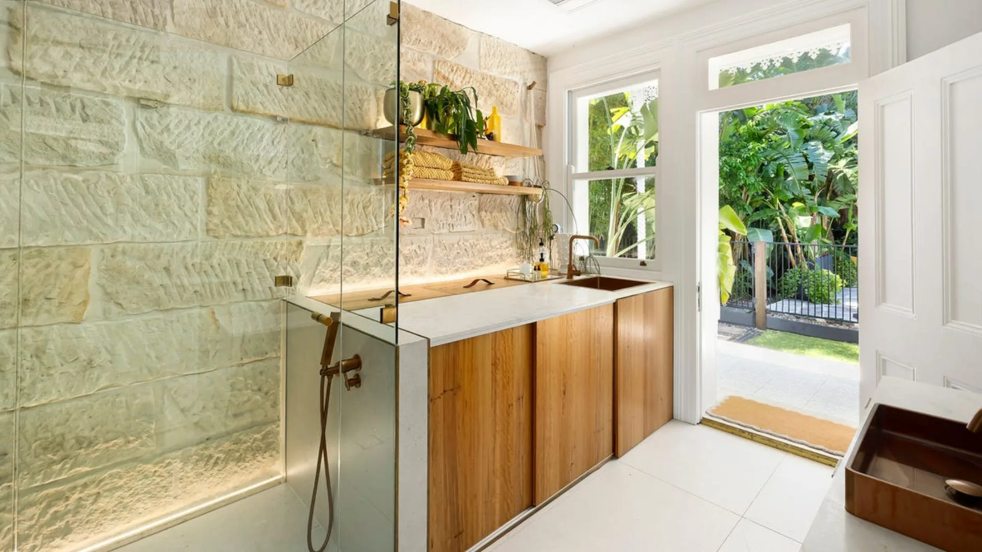 John Aiken's bathroom with raw sandstone feature wall, timber cabinets and copper tapware.