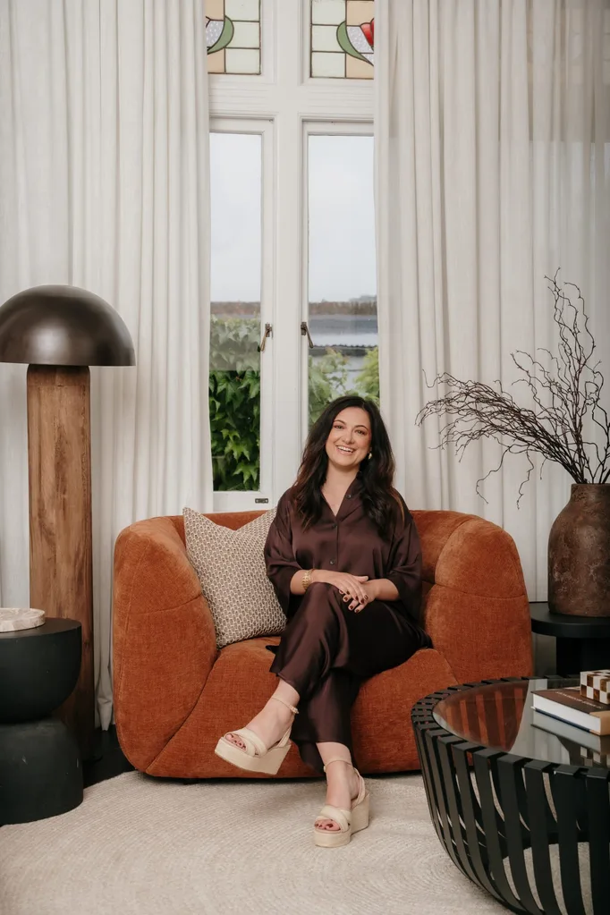 an Australian designer sitting on an orange sofa in a stylish room with a window, modern lamp, and decorative vases.