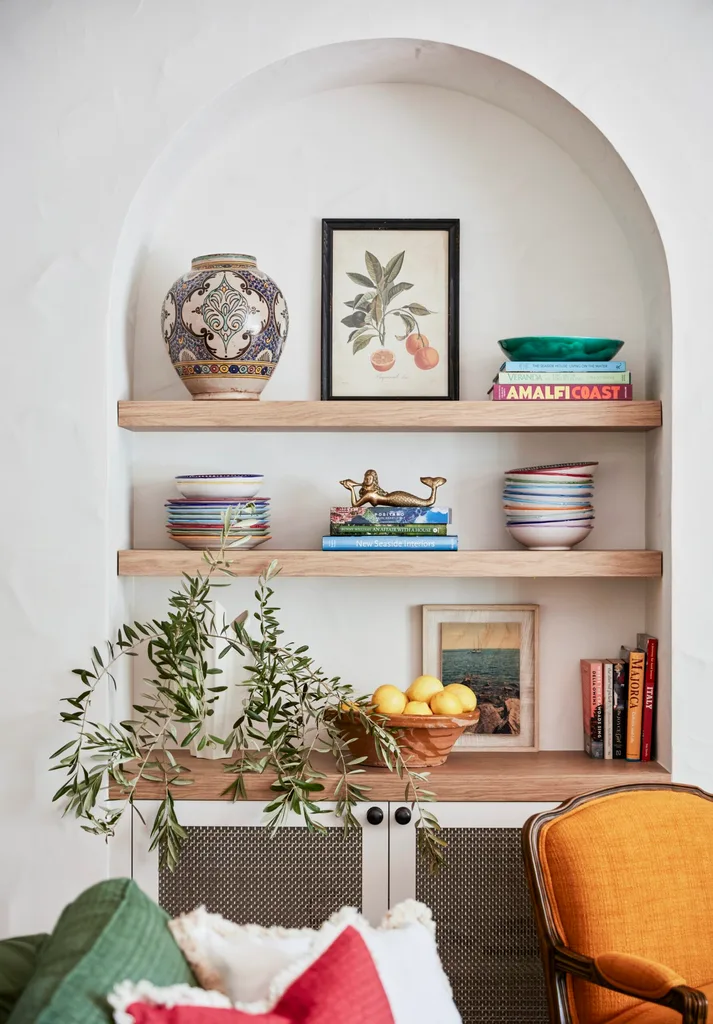 Built-in arched alcove with timber open shelves decorated with books, decorative plates, a vase, a plant, and a bowl of lemons.
