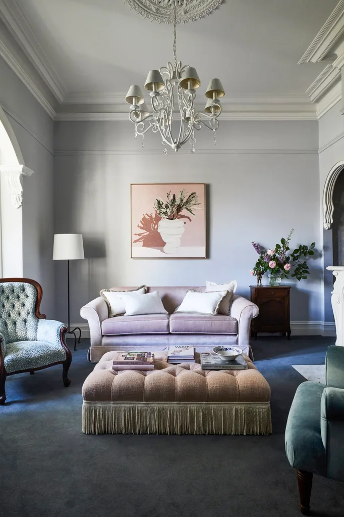 Elegant living room with a chandelier, pink sofa, blue armchair, and coffee table with books, under framed wall art. fringe decor trend