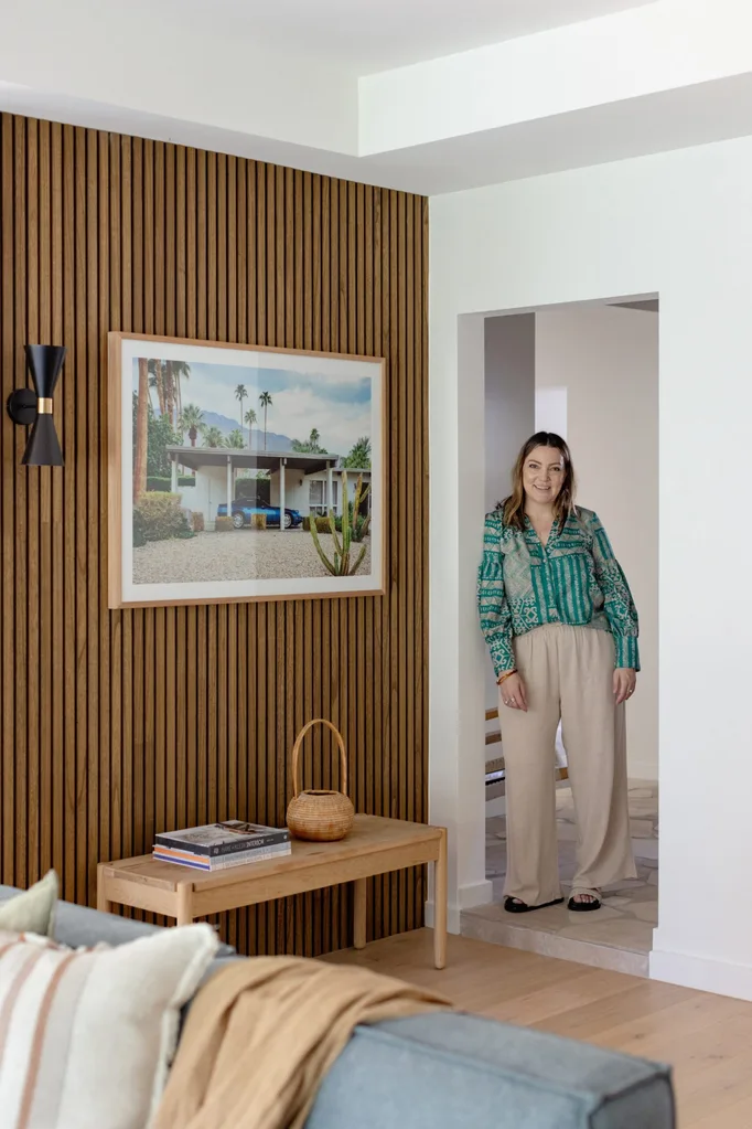 an Australian designer in a green patterned shirt stands in a modern living room with wood paneling and a large framed photo.