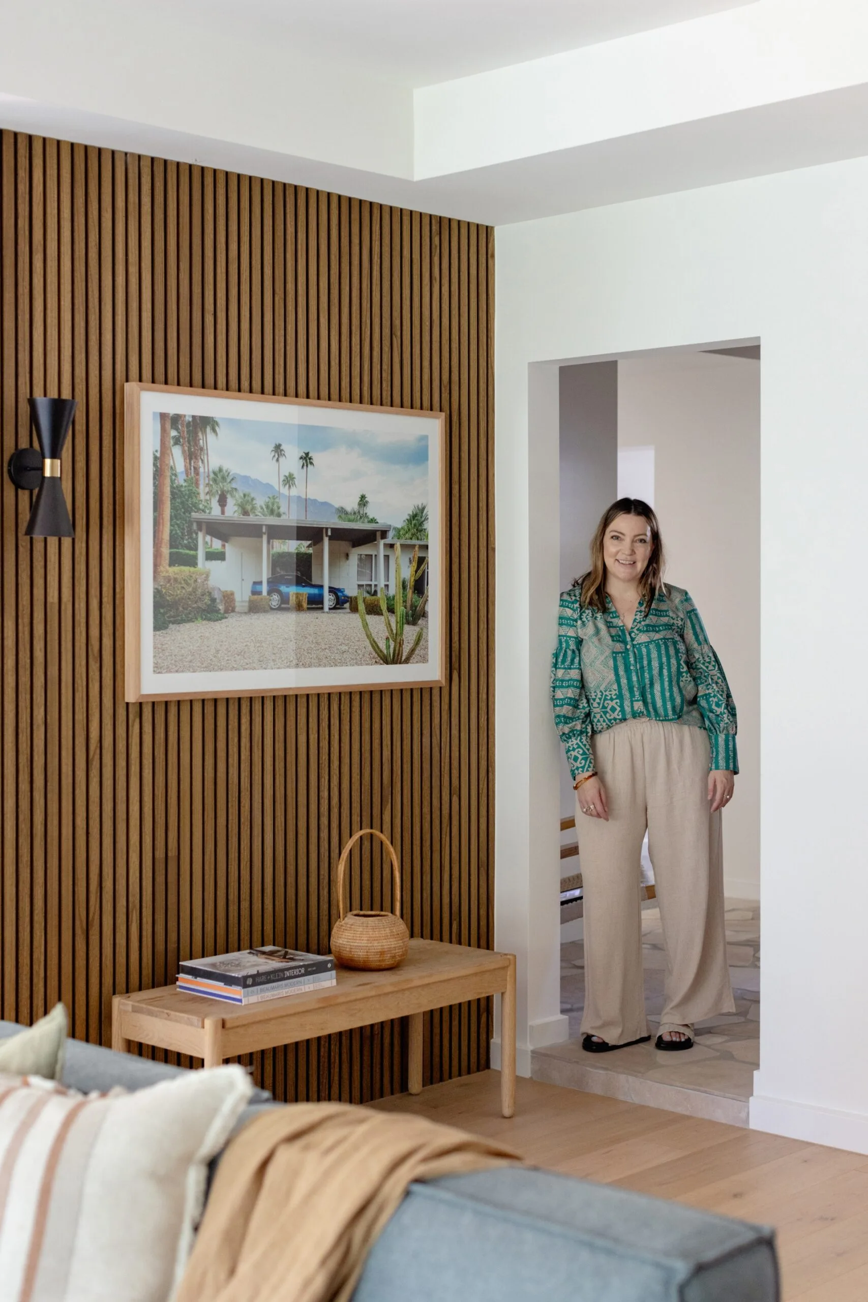 an Australian designer in a green patterned shirt stands in a modern living room with wood paneling and a large framed photo.