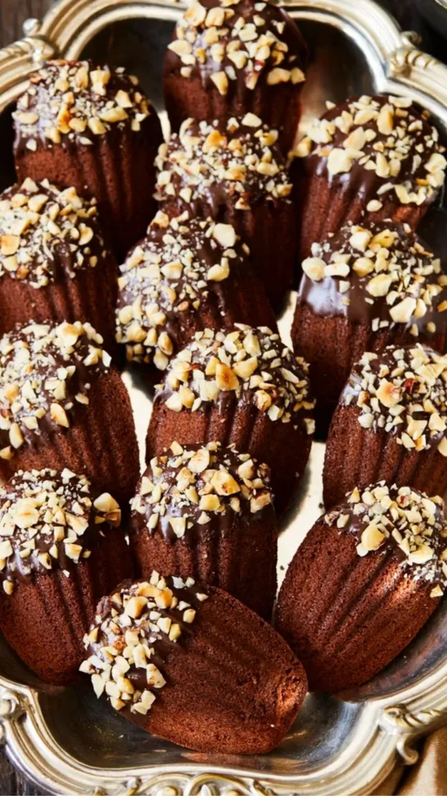 chocolate madeleines dipped in chocolate and crushed nuts displayed on a decorative silver tray