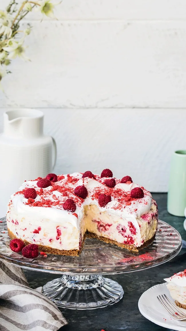 eton mess cheesecake decorated with fresh raspberries on a cake stand