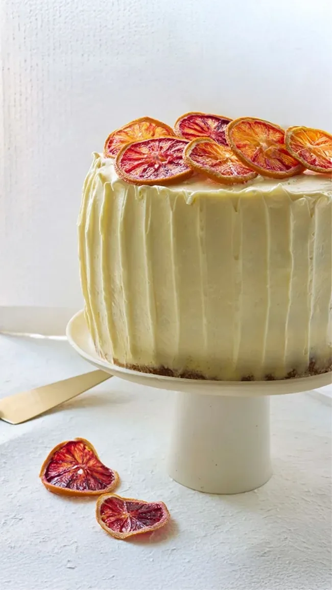 Mimosa cake with yellow icing and candied orange decorations on a white cake stand