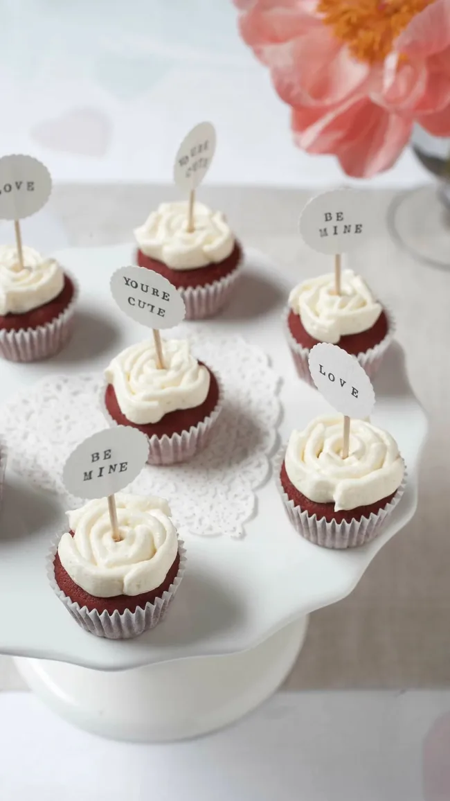 Raspberry red velvet mini cupcakes displayed on table with heart doily and pink flowers for Valentine's Day