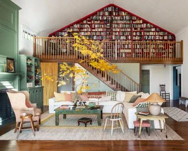 Cozy living room with white sofas, vibrant cushions, a green bookcase, and a loft library with red shelving.