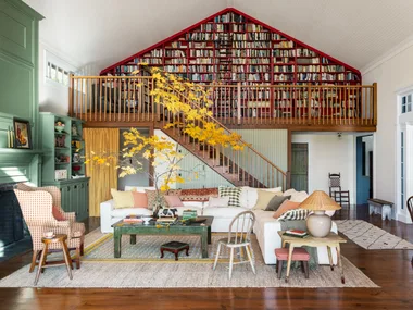 Cozy living room with white sofas, vibrant cushions, a green bookcase, and a loft library with red shelving.