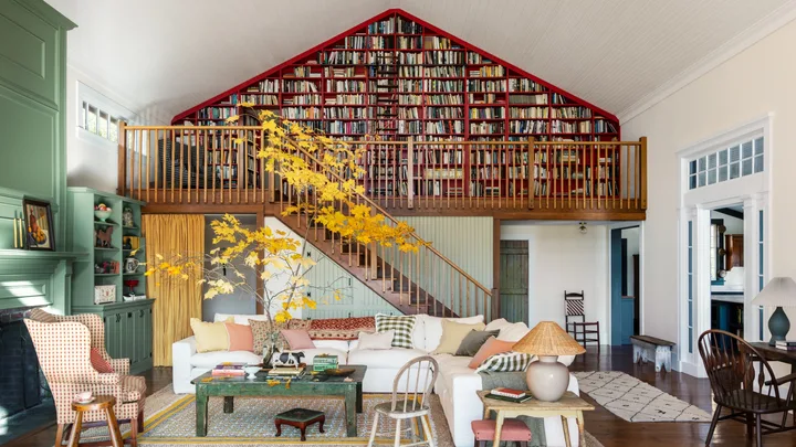 Cozy living room with white sofas, vibrant cushions, a green bookcase, and a loft library with red shelving.