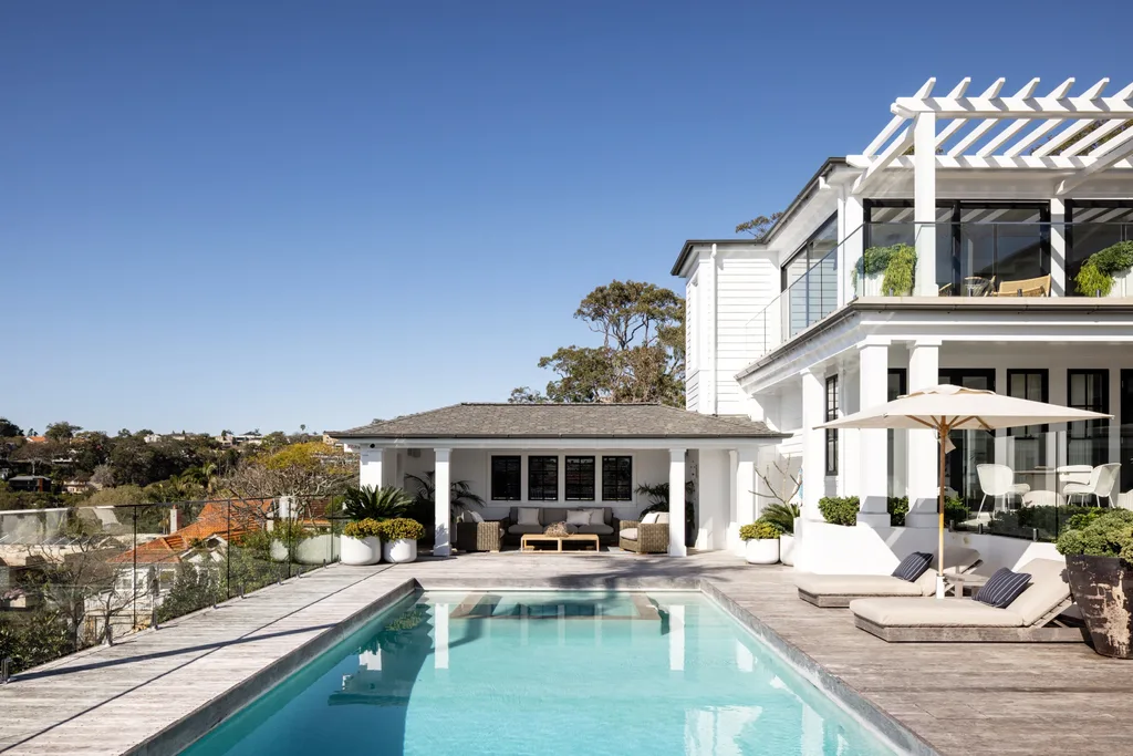 Luxurious house with a spacious patio, swimming pool, sun loungers, and pergola under a clear blue sky.