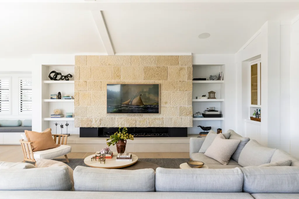 Spacious living room in a fully redesigned and renovated heritage home with stone fireplace, large grey L-shaped sofas, and artwork of a sailboat on the wall. The artwork is actually a television that gives the appearance of a painting when not in use.