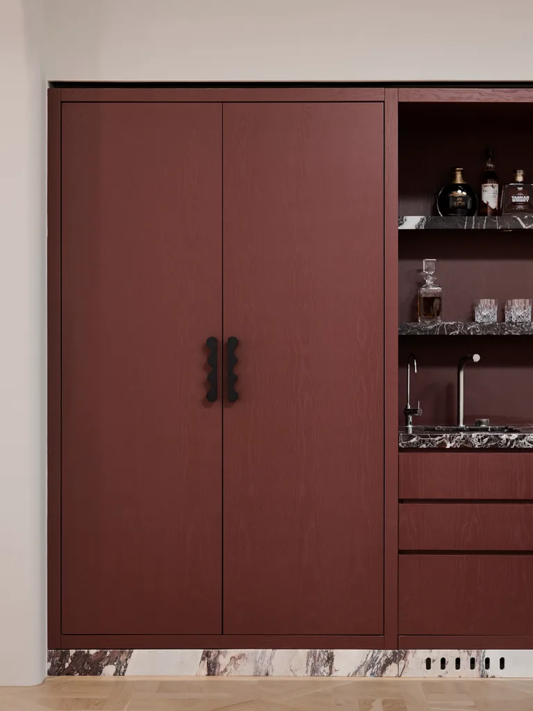 A close up photo of burgundy coloured joinery, with a black handle. The joinery is comprised of a tall cupboard, with drawers beside it and open shelves. The material used on the open shelves is a dramatic burgundy colour marble with white veining.