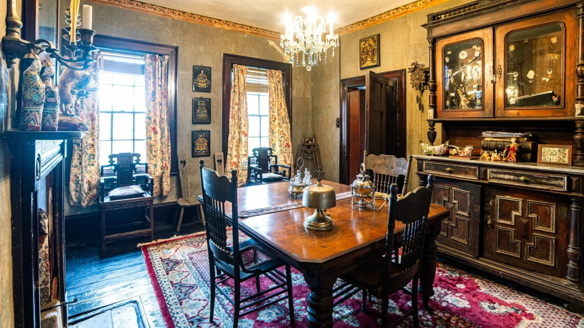 Dining room inside a Georgian house with chandelier, dark wood furniture, floral curtains, and decorative items on shelves.