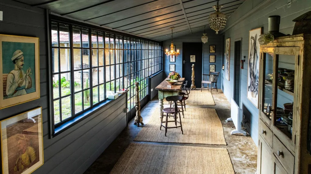 Blue hallway with large windows inside a Georgian house , wooden furniture, hanging lights, artwork on walls, and woven rugs.