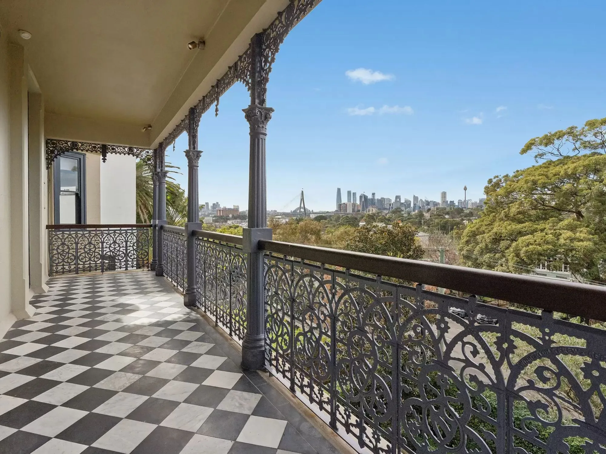 The black and white tiled balcony with wrought-iron lacework and views of the Sydney CBD from Annandale historic house