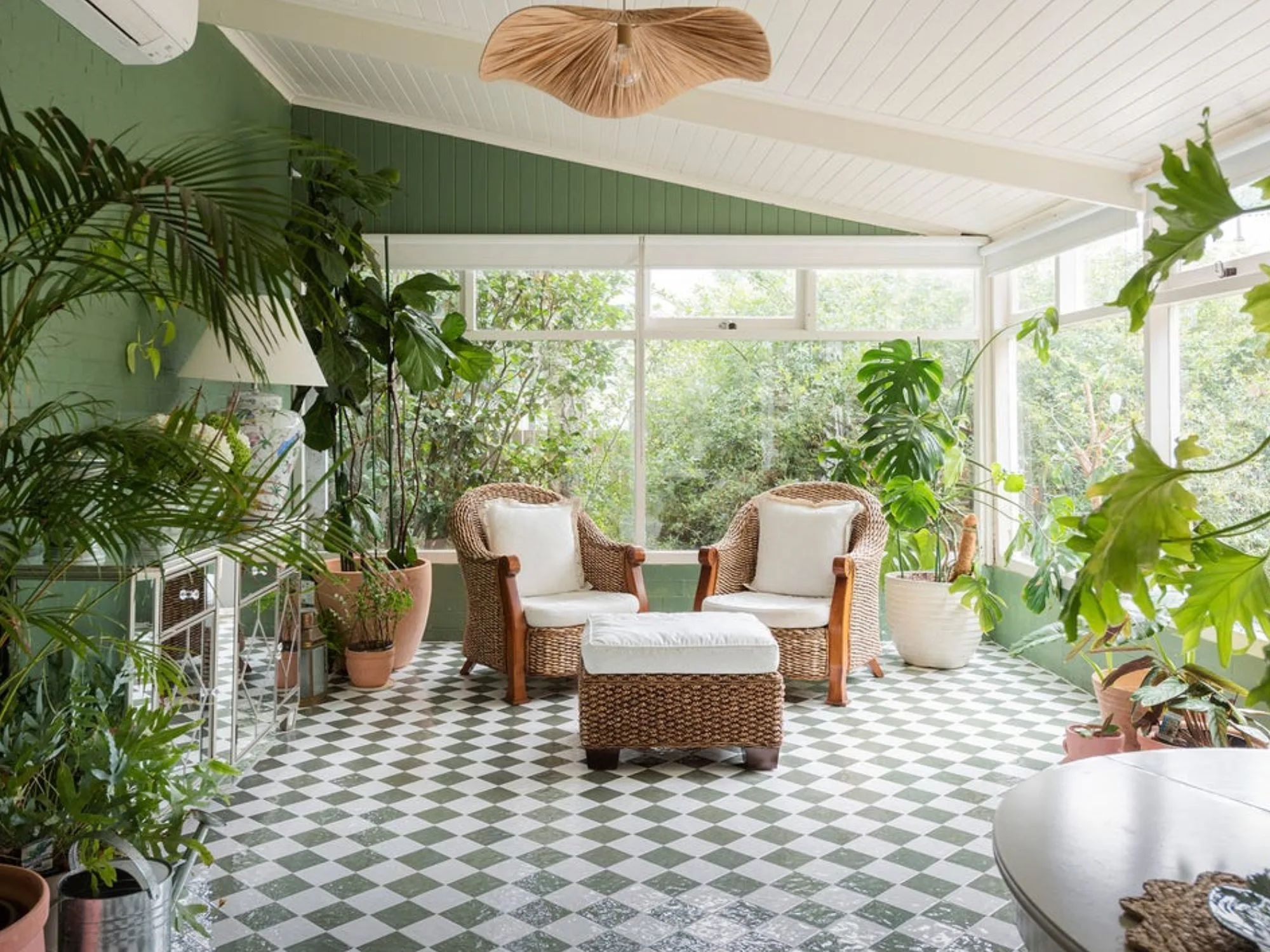 An indoor conservatory with green and white floor tiles, green walls, large windows on one side and a cream and rattan living set