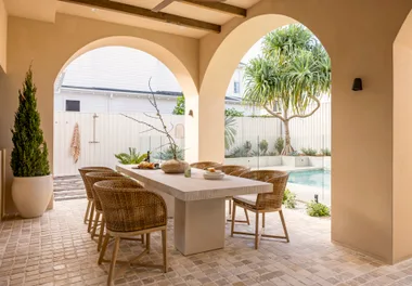 Stylish outdoor dining area with wicker chairs, stone table, and pool view under archways.
