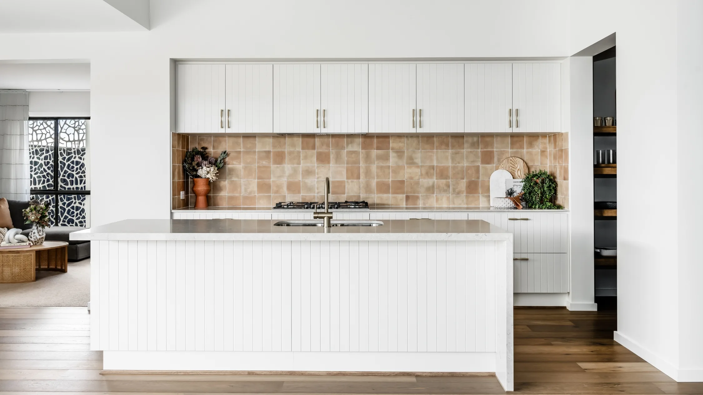 White kitchen with tongue and groove style cabinetry, waterfall stone kitchen island and square terracotta tile splashback
