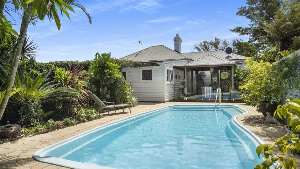 an inground pool in the backyard of a white weatherboard cottage