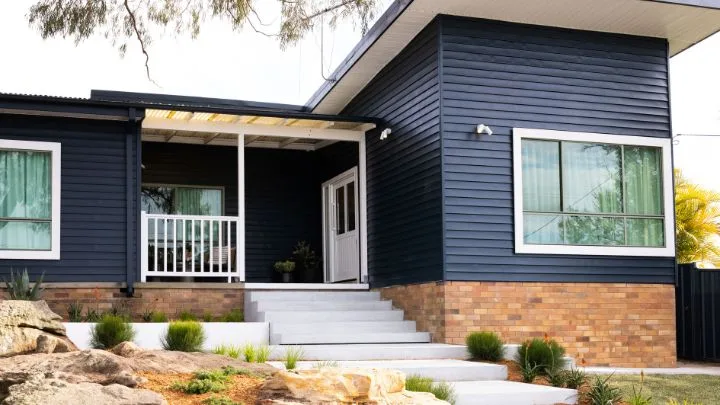 The after image of an Edmonson Park home after its Selling Houses Australia makeover, with black boards, white window frames and fencing, new concrete stairs and landscaped garden. 