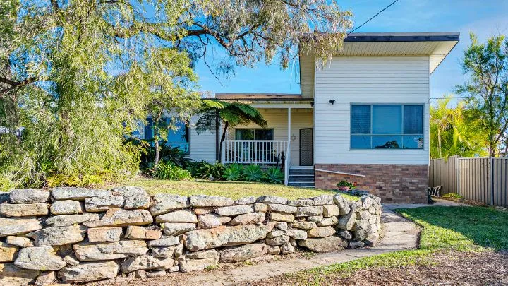 A before image of an old cream weatheboard home in Edmonson Park with a rough sandstone retaining wall