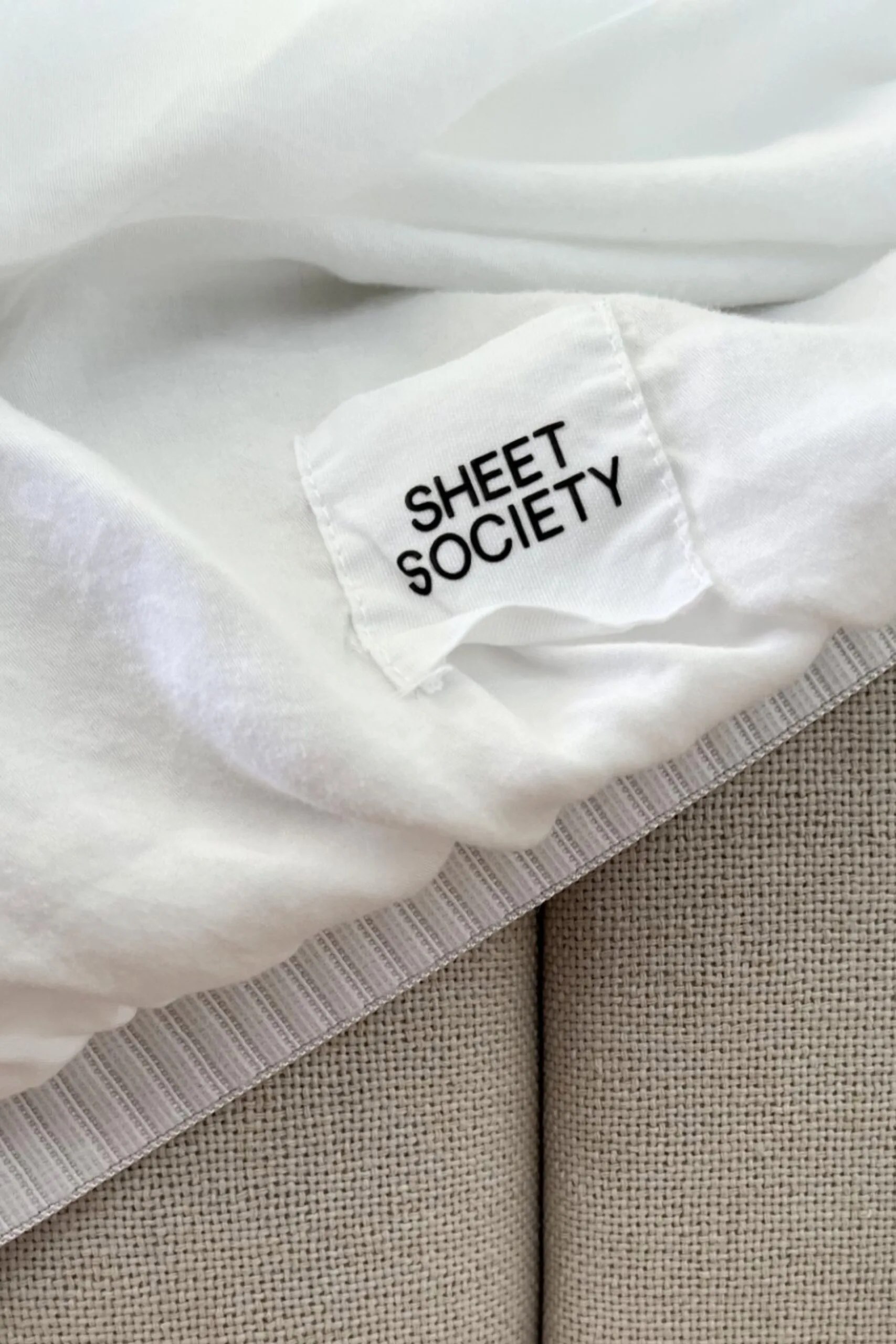 Close-up of Sheet Society white bamboo sheets and a beige fabric bedhead.