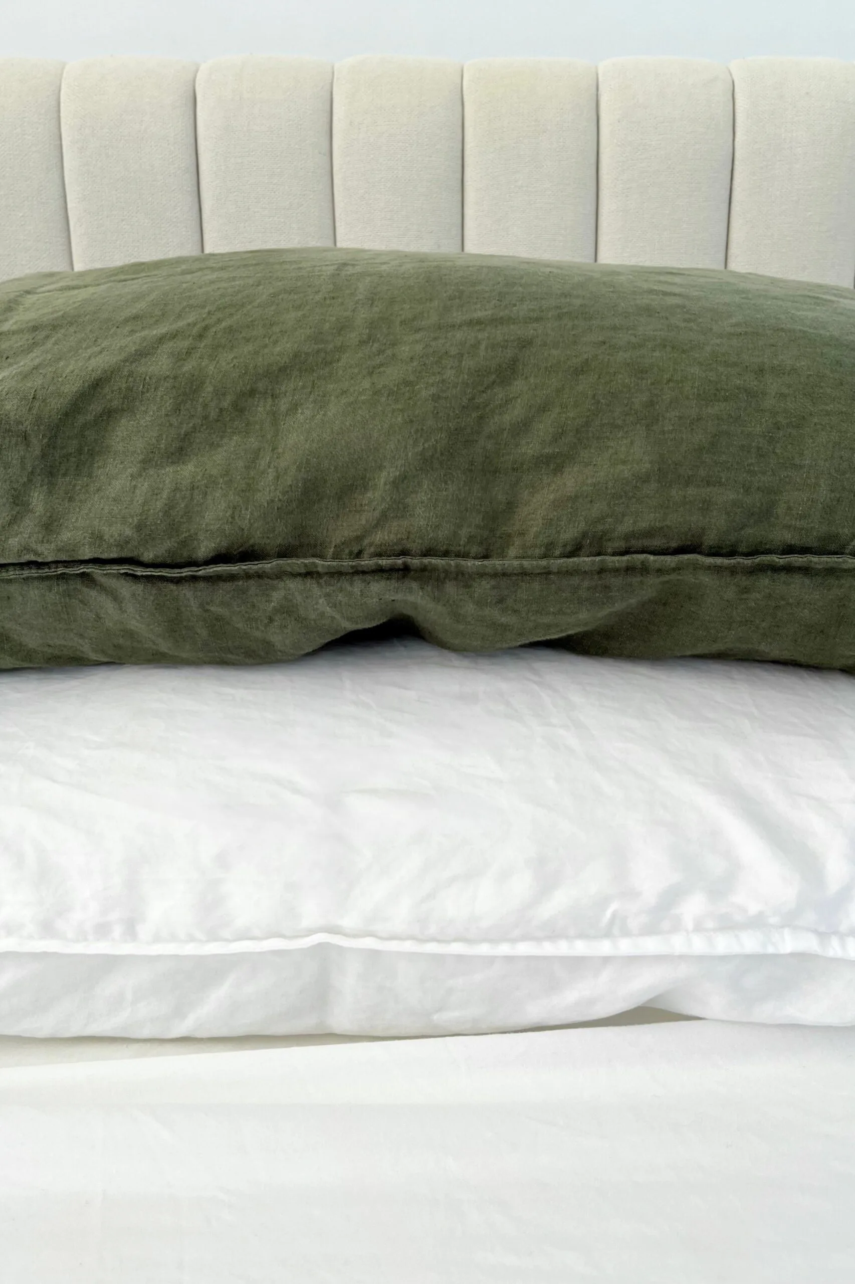 Olive green linen pillows, white bamboo sheets and a beige fabric bedhead.