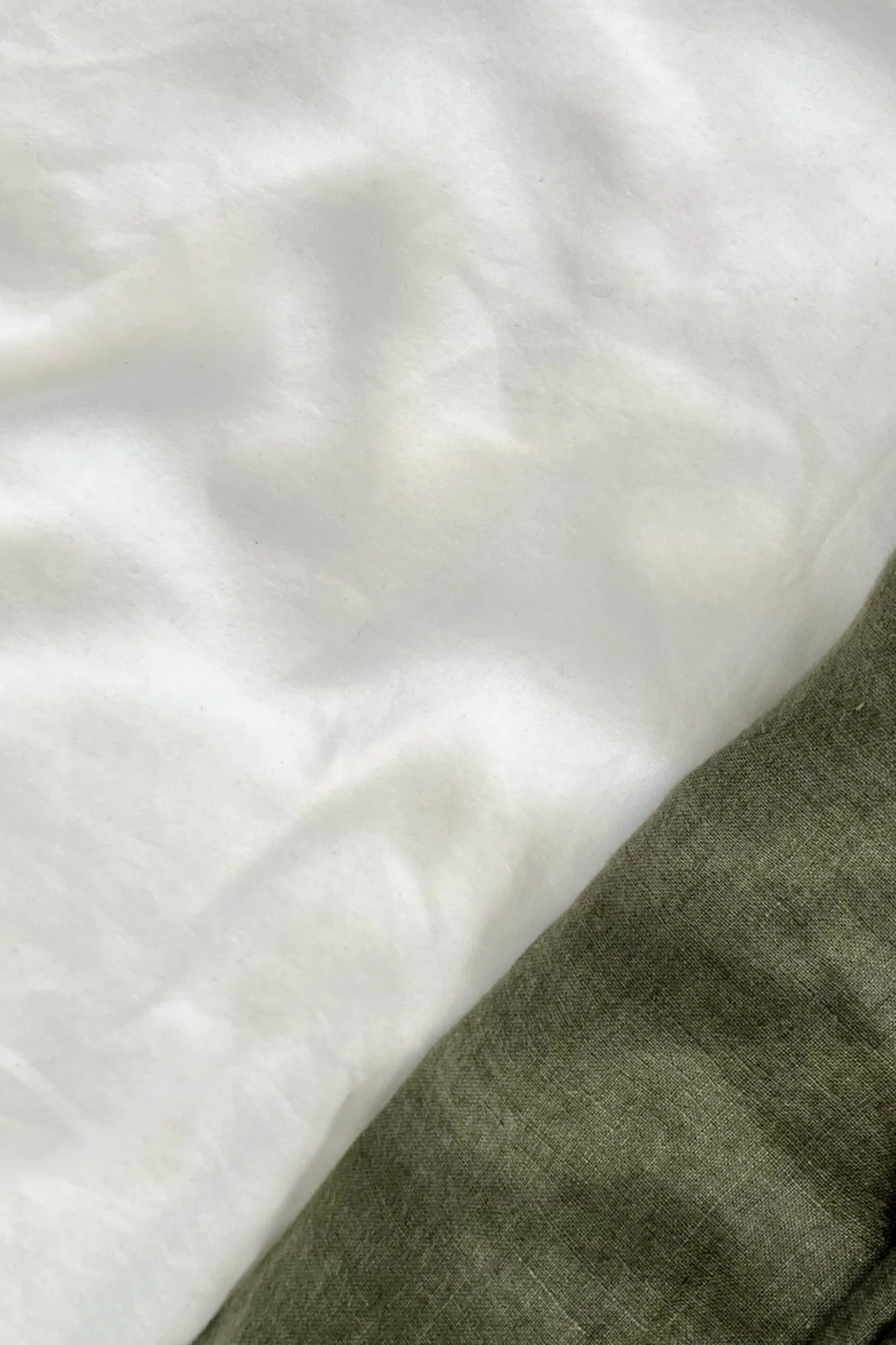 Close-up of white bamboo sheets and olive green linen bedlinen.
