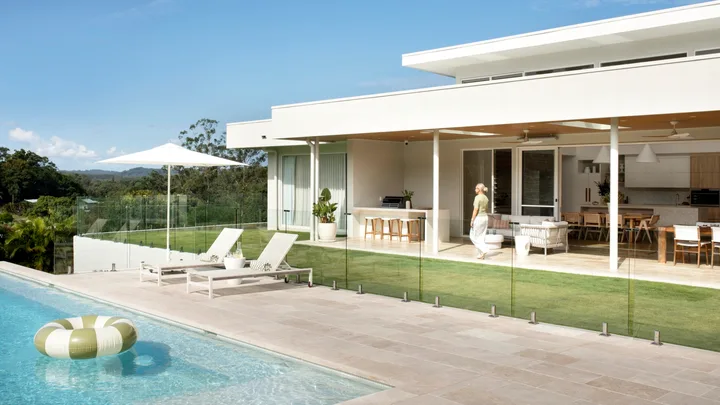 Modern house with glass doors, poolside loungers, umbrella, and inflatable ring in a clear sky setting.
