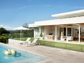 Modern house with glass doors, poolside loungers, umbrella, and inflatable ring in a clear sky setting.