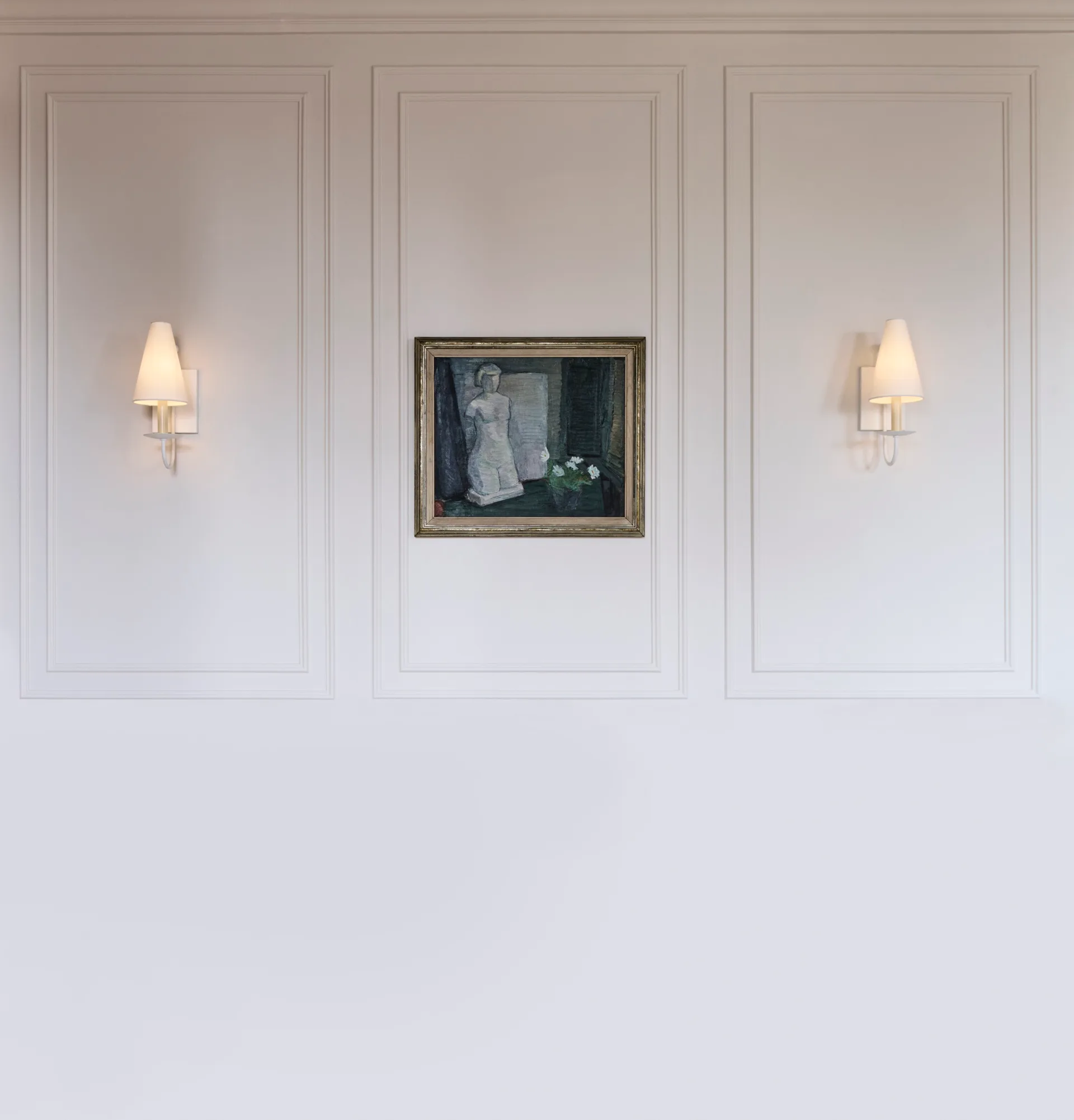 A white wall with decorative panelling, a still life painting of a sculpture and flower in the middle, and two wall sconces on either side.